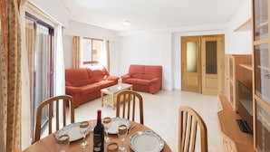 A compact living room with two red sofas, a dining table set with plates and wine glasses, and a TV on a wooden cabinet. - NAVEGANTE - Apartment with shared pool in Playa de Gandia. (Playa de Gandia)