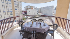 A balcony with a round table set for four, surrounded by chairs, overlooking a cityscape with buildings and a street. - NAVEGANTE - Apartment with shared pool in Playa de Gandia. (Playa de Gandia)