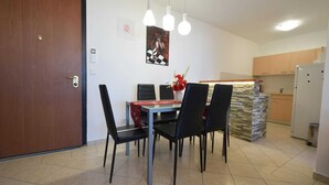 A dining area with a table, chairs, and hanging lights. There is a kitchen area with cabinets and a refrigerator in the background. - Apartment Lucy with a Balcony (Vantačići)
