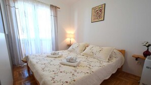 A bedroom with a floral bedspread, two pillows, a bedside table with a lamp, and a wall-mounted picture. - Apartment Lucy with a Balcony (Vantačići)