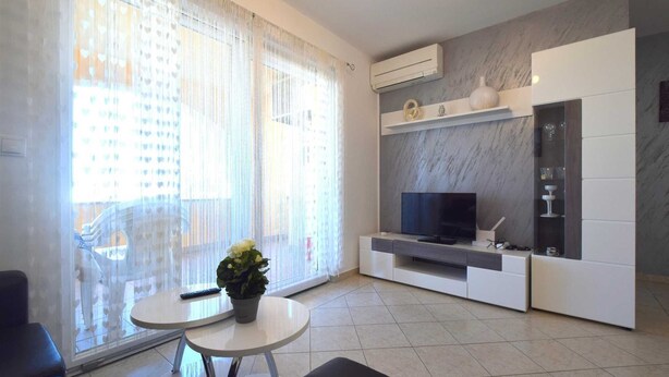 A modern living room with a flat-screen TV, a small table with a potted plant, and a sofa. - Apartment Lucy with a Balcony (Vantačići)