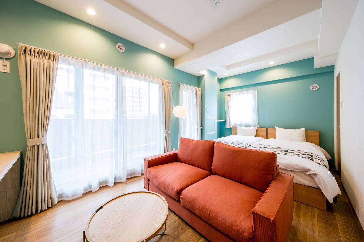 A modern hotel room with a wooden floor, a red sofa, a round wooden table, and a bed with white bedding.