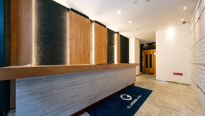 Una zona de recepción con un mostrador de madera, un felpudo azul oscuro con el logotipo del hotel y un diseño de interiores moderno.