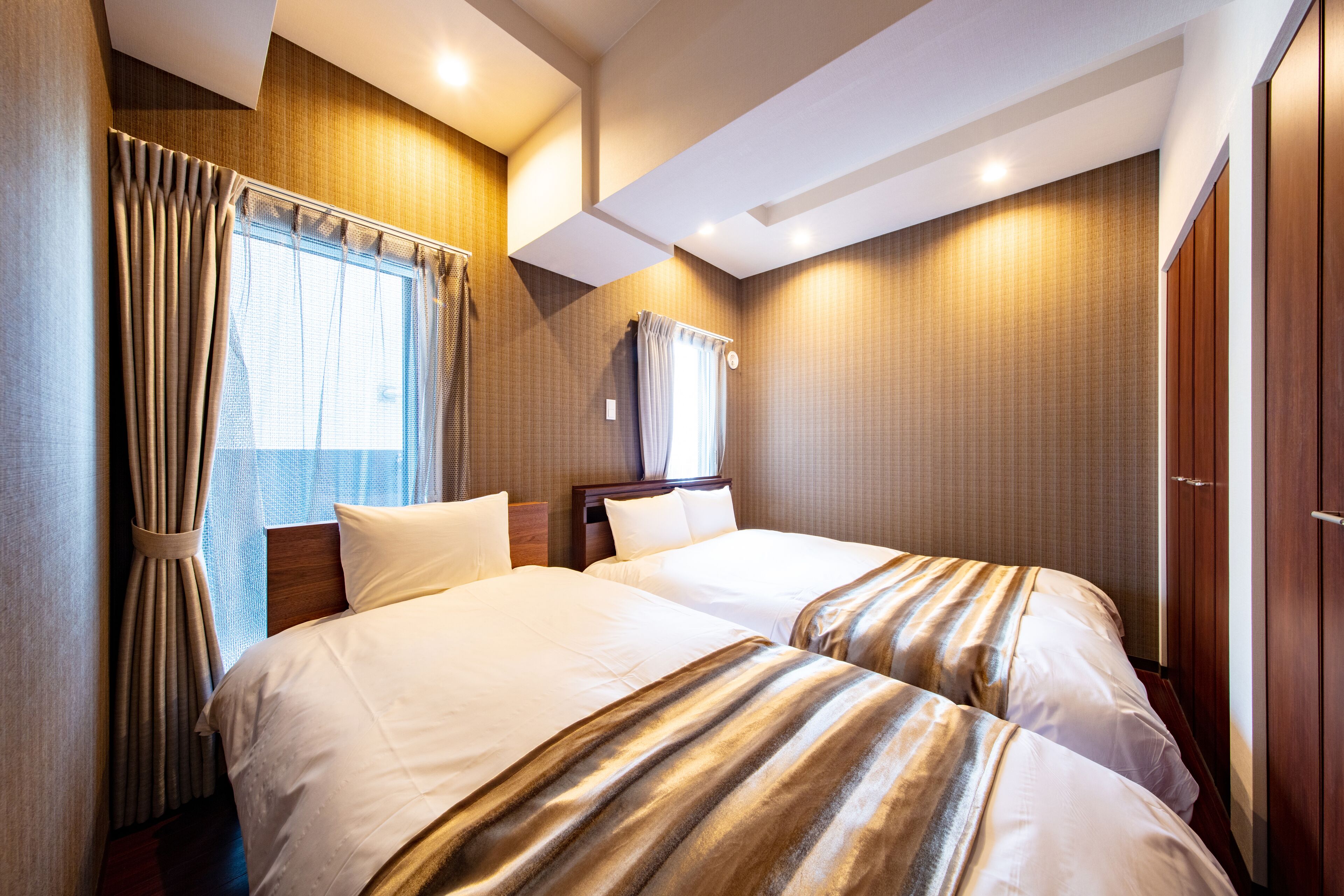 A hotel room with two beds, a wooden wardrobe, and a window with curtains.