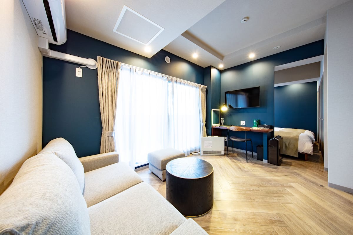 A modern hotel room with a sofa, a round coffee table, a desk with a chair, and a bed.