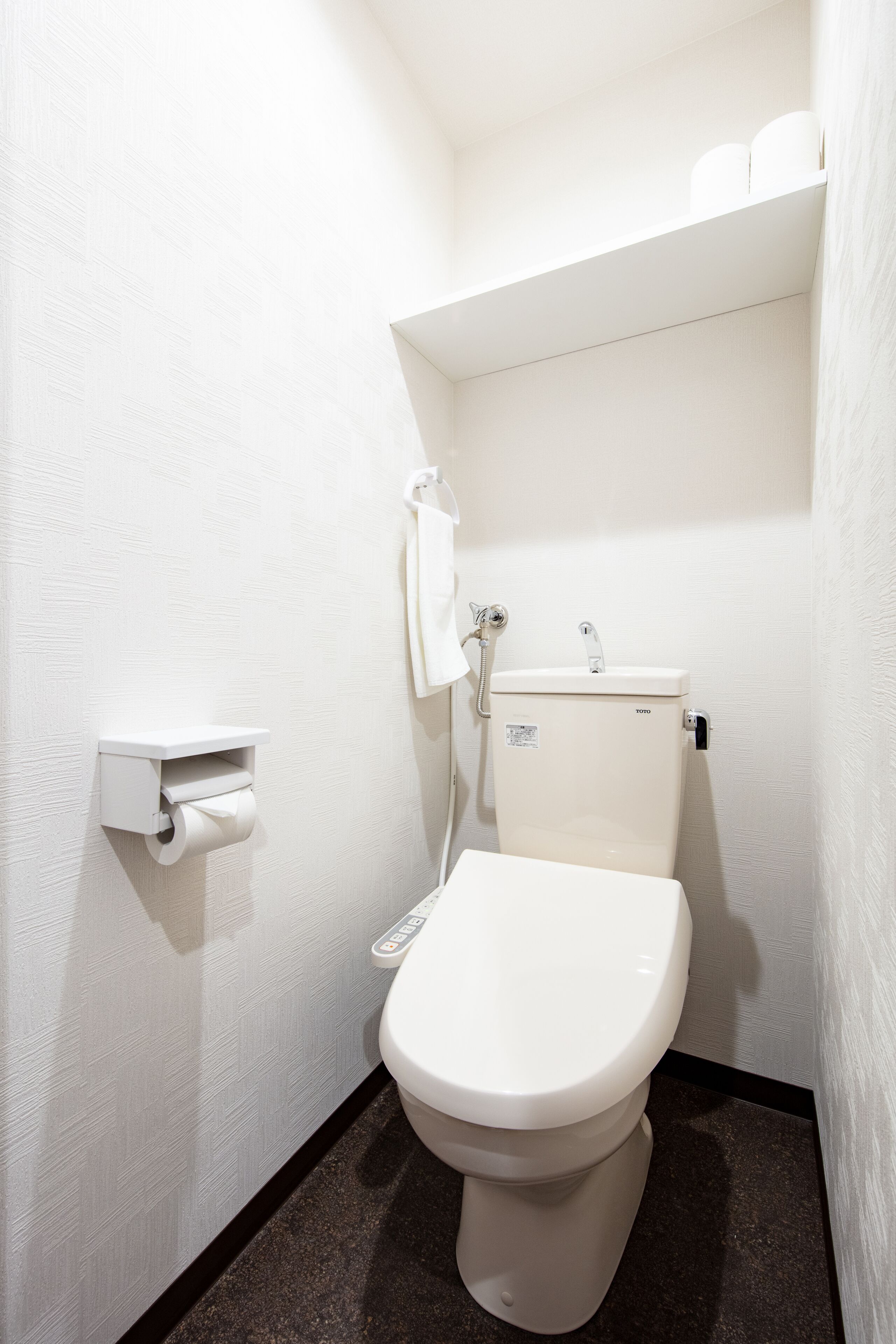 A small, white bathroom with a toilet, a paper towel dispenser, and a towel rack.