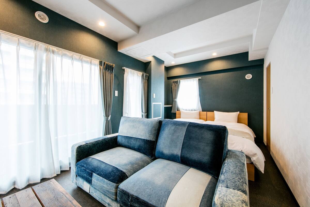 A modern hotel room with a sofa, a bed, and a large window with curtains.