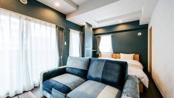 Una habitación de hotel moderna con sofá, cama y un gran ventanal con cortinas.