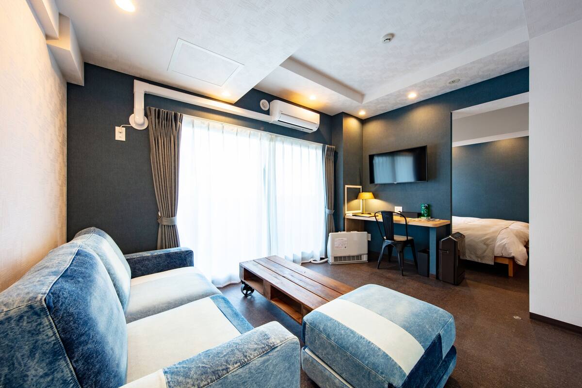 A modern hotel room with a sofa, a desk, a bed, and a TV.