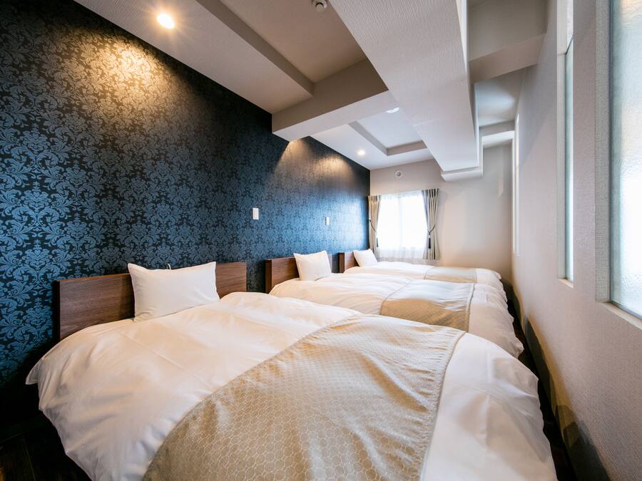 A hotel room with two beds, a patterned wallpaper, and a window with curtains.