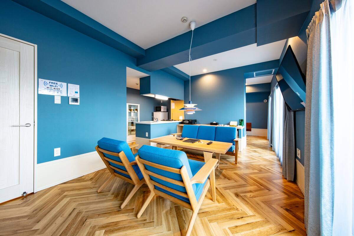 A modern dining area with blue walls, wooden flooring, and blue chairs.