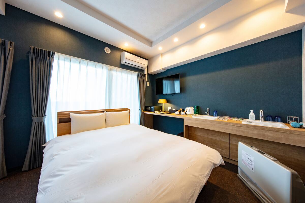 A hotel room with a large bed, a desk with a sink, a mirror, and an air conditioning unit.