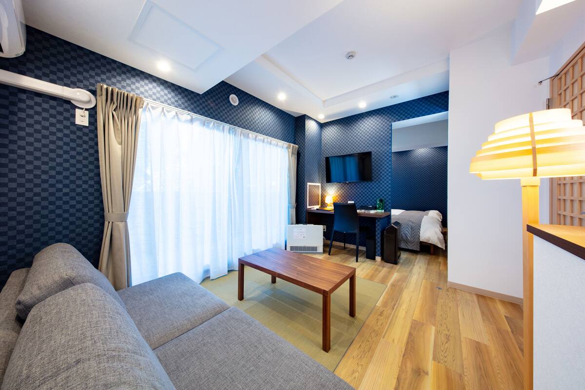 A modern living room with a sofa, a wooden coffee table, a desk with a chair, and a TV mounted on the wall.
