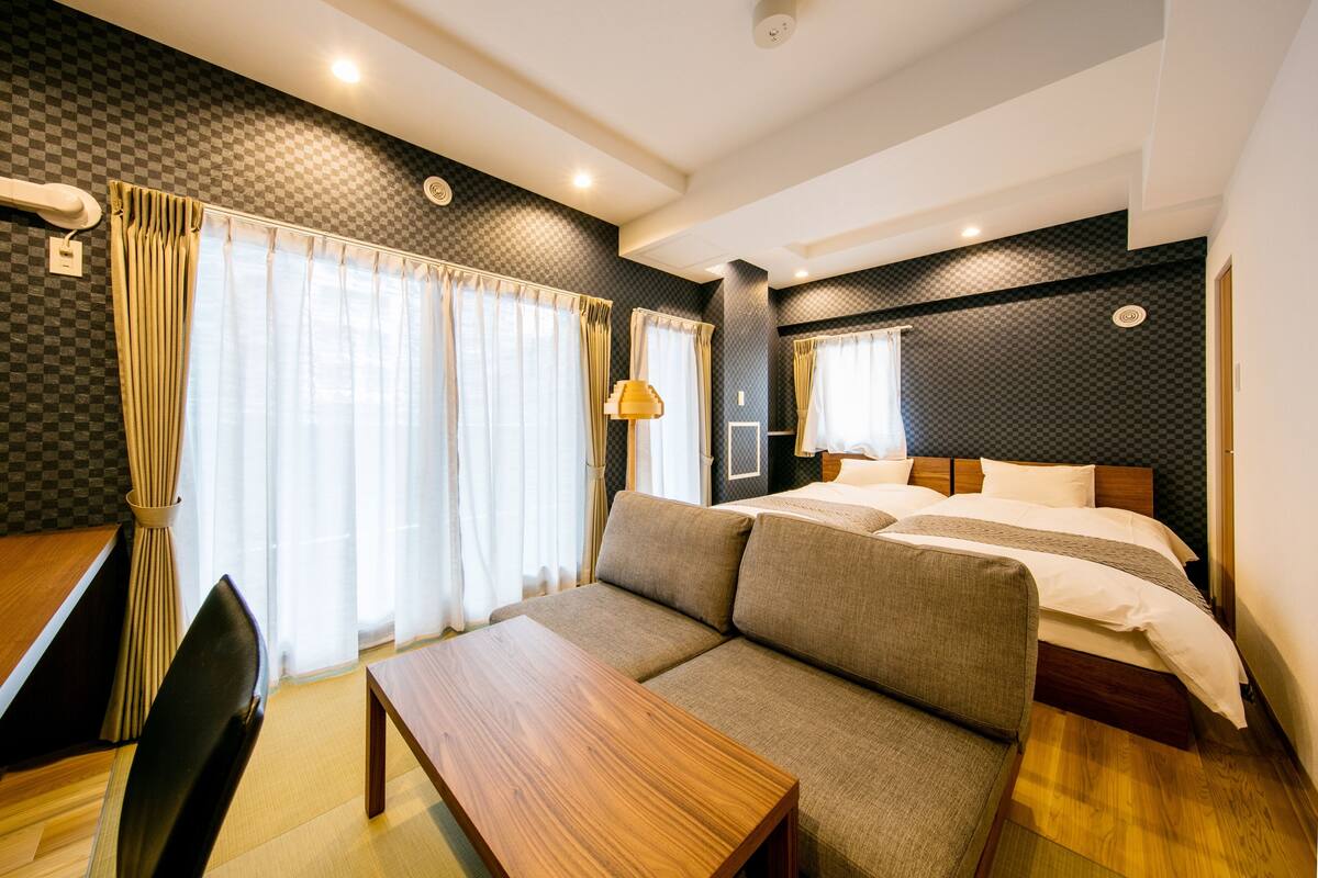 A modern hotel room with a sofa, a wooden table, a bed, and a window with curtains.