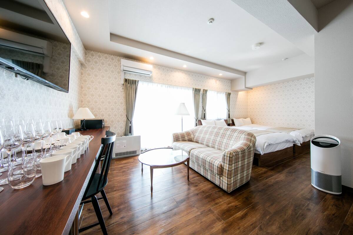 A hotel room with a wooden floor, a sofa, a bed, a TV, and a table with glasses.