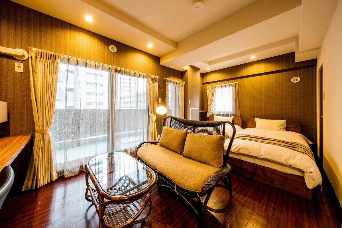 A hotel room with a bed, a sofa, a table, and a window with curtains.