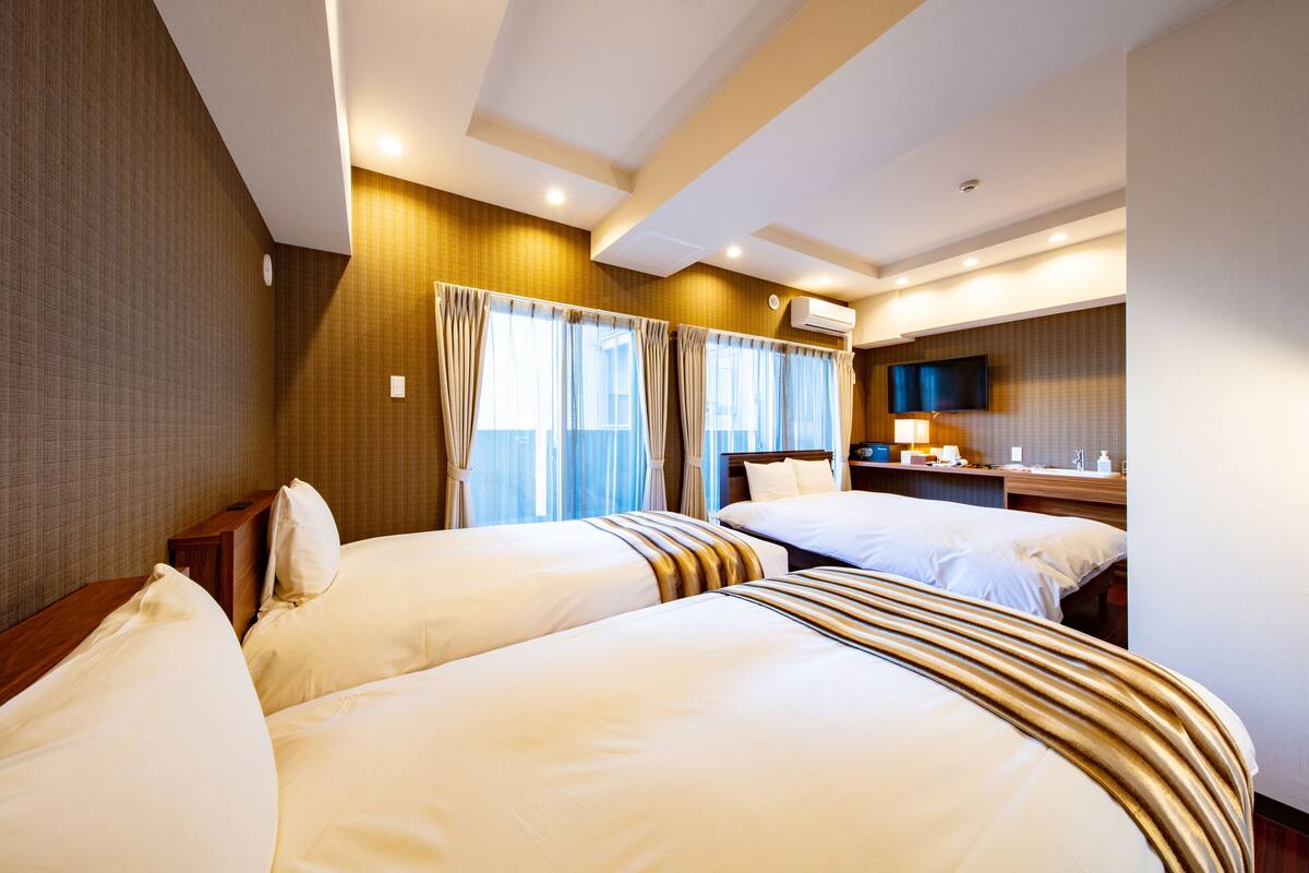 A hotel room with two beds, a TV, a bedside table, and a window with curtains.