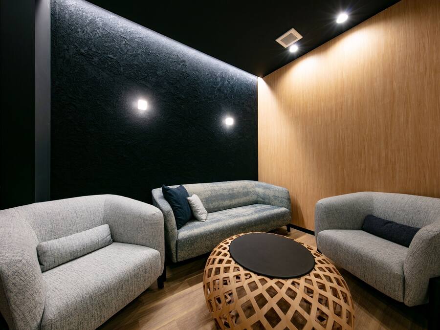 Un espace de détente moderne avec des canapés gris, un mur d’accent en bois et une table ronde en bois.