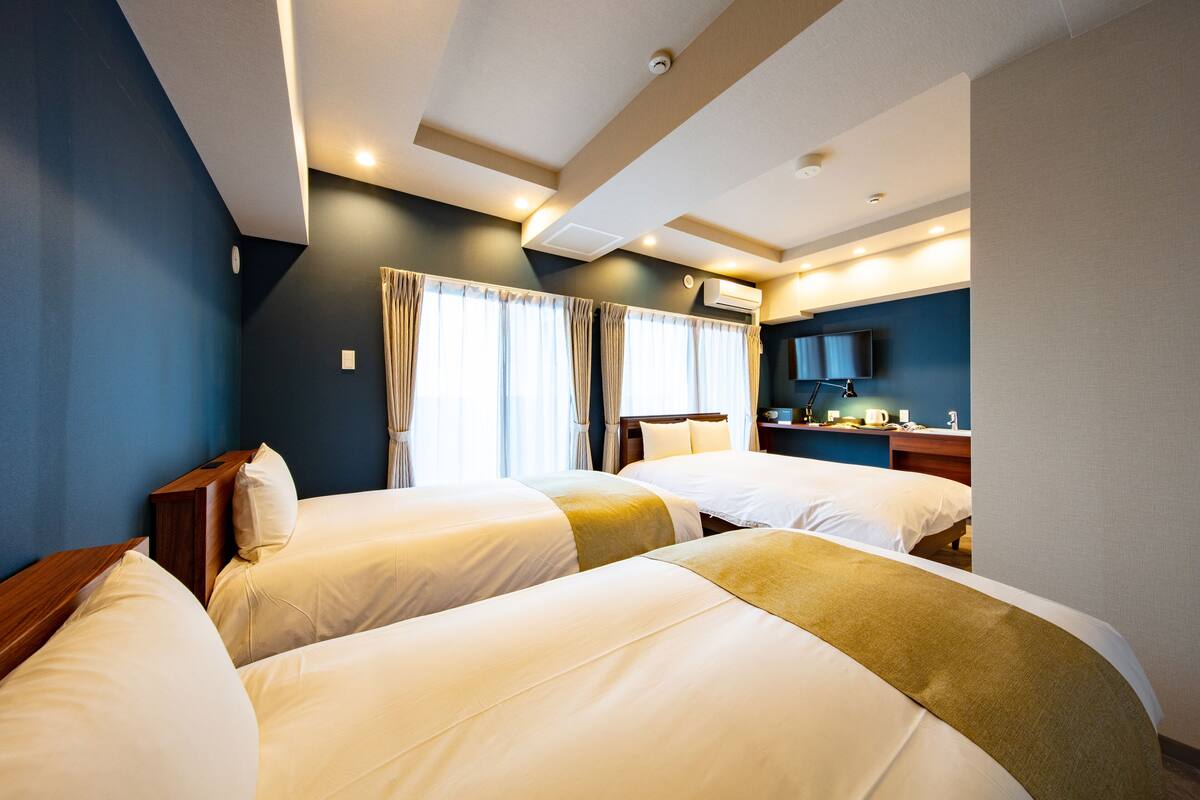 A hotel room with two beds, a flat-screen TV, a desk, and a window with curtains.