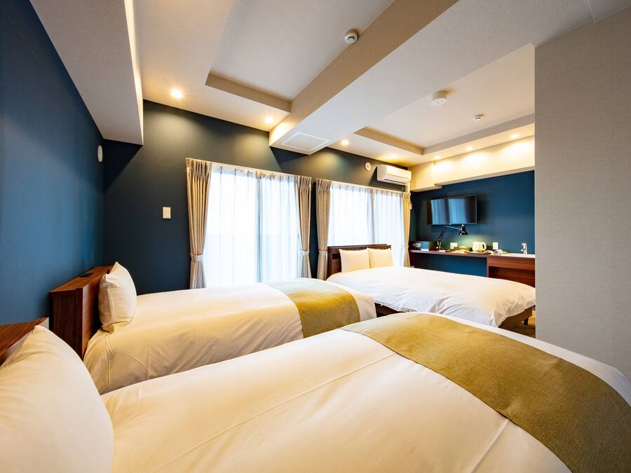 A hotel room with two beds, a flat-screen TV, a desk, and a window with curtains.