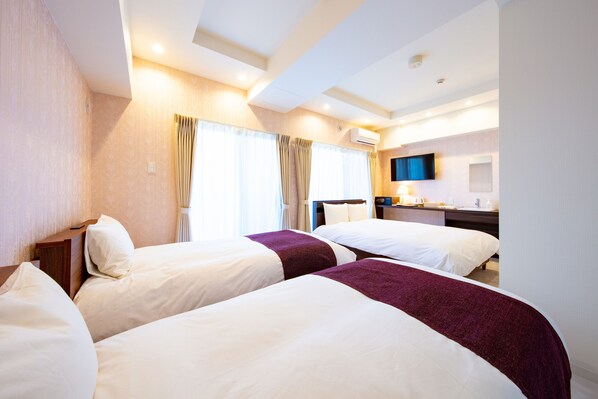 A hotel room with two beds, a desk, a TV, and a bathroom.