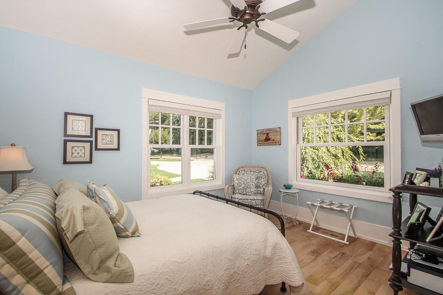 A bedroom with a bed, a chair, a TV, and two windows.