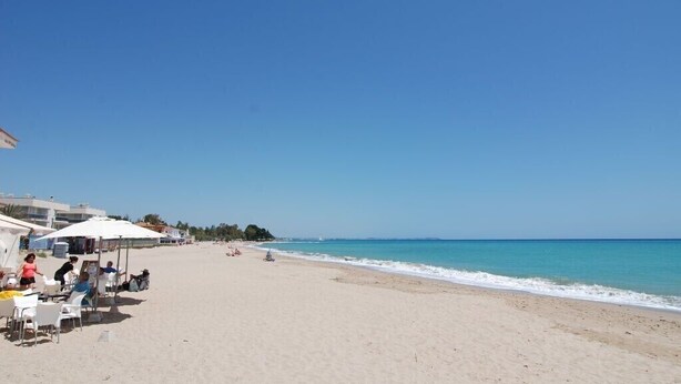 Una zona sulla spiaggia con posti a sedere all'aperto e ombrelloni, cielo sereno e mare calmo.