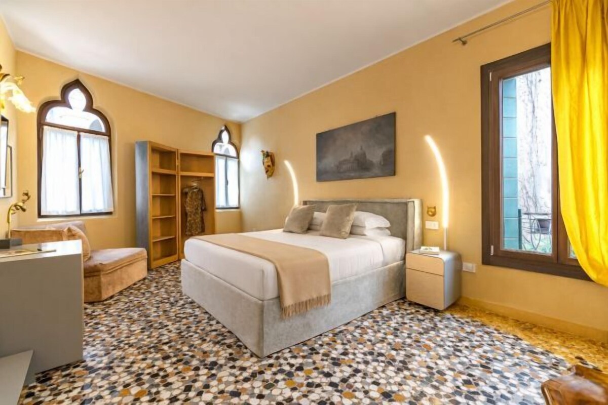 A bedroom with a bed, bedside tables, a desk, a chair, a window with curtains, and a patterned floor.