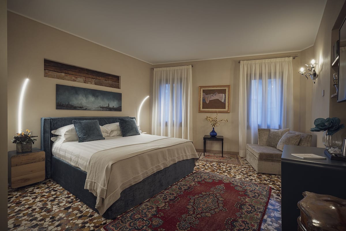 Ein Schlafzimmer mit einem großen Bett, einem Nachttisch, einem Sessel, einem Schreibtisch und einem Fenster mit Vorhängen.