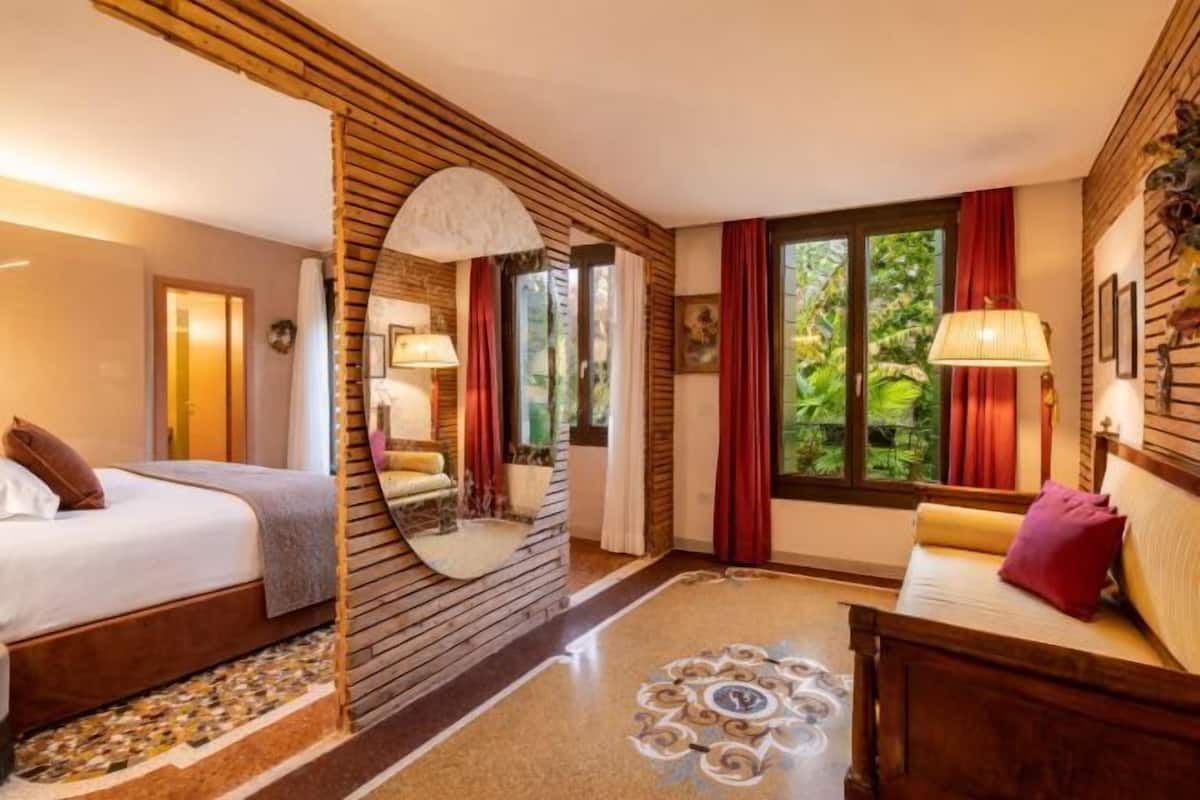 Ein Hotelzimmer mit Bett, einer Couch, einem Spiegel und einem Fenster mit Vorhängen.