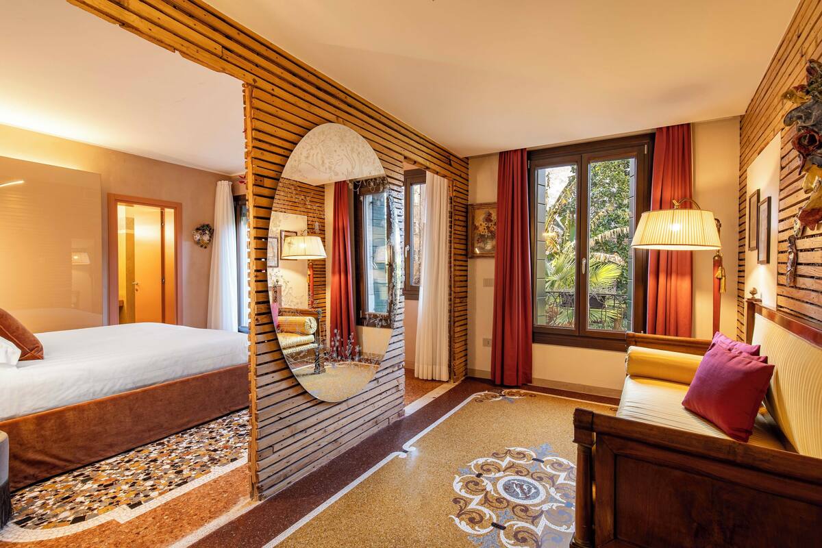 Ein Hotelzimmer mit Bett, Sofa, Spiegel und einem Fenster mit Vorhängen.