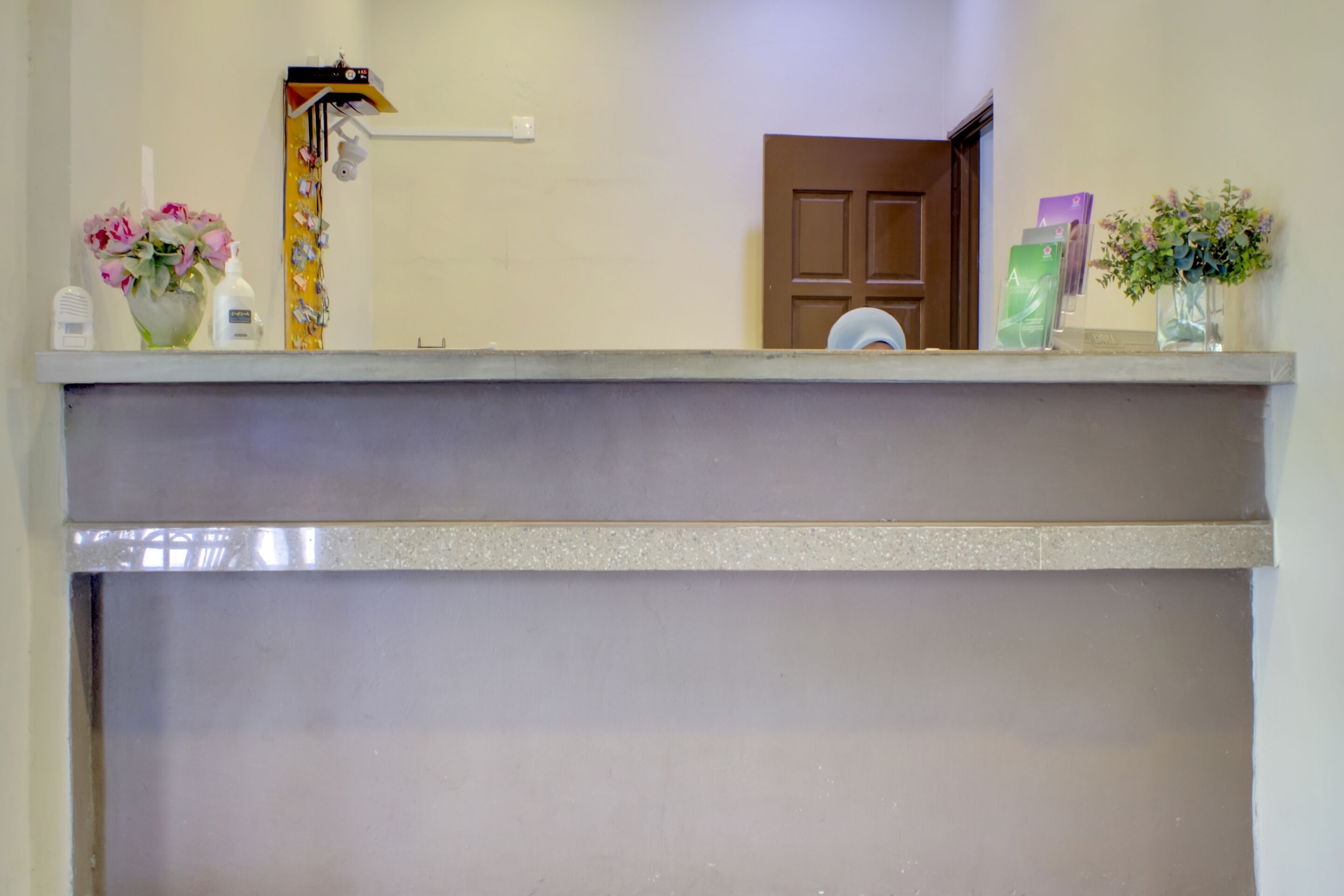 A reception area with a counter, a door, and various items like a vase with flowers, a bottle, and some cards.