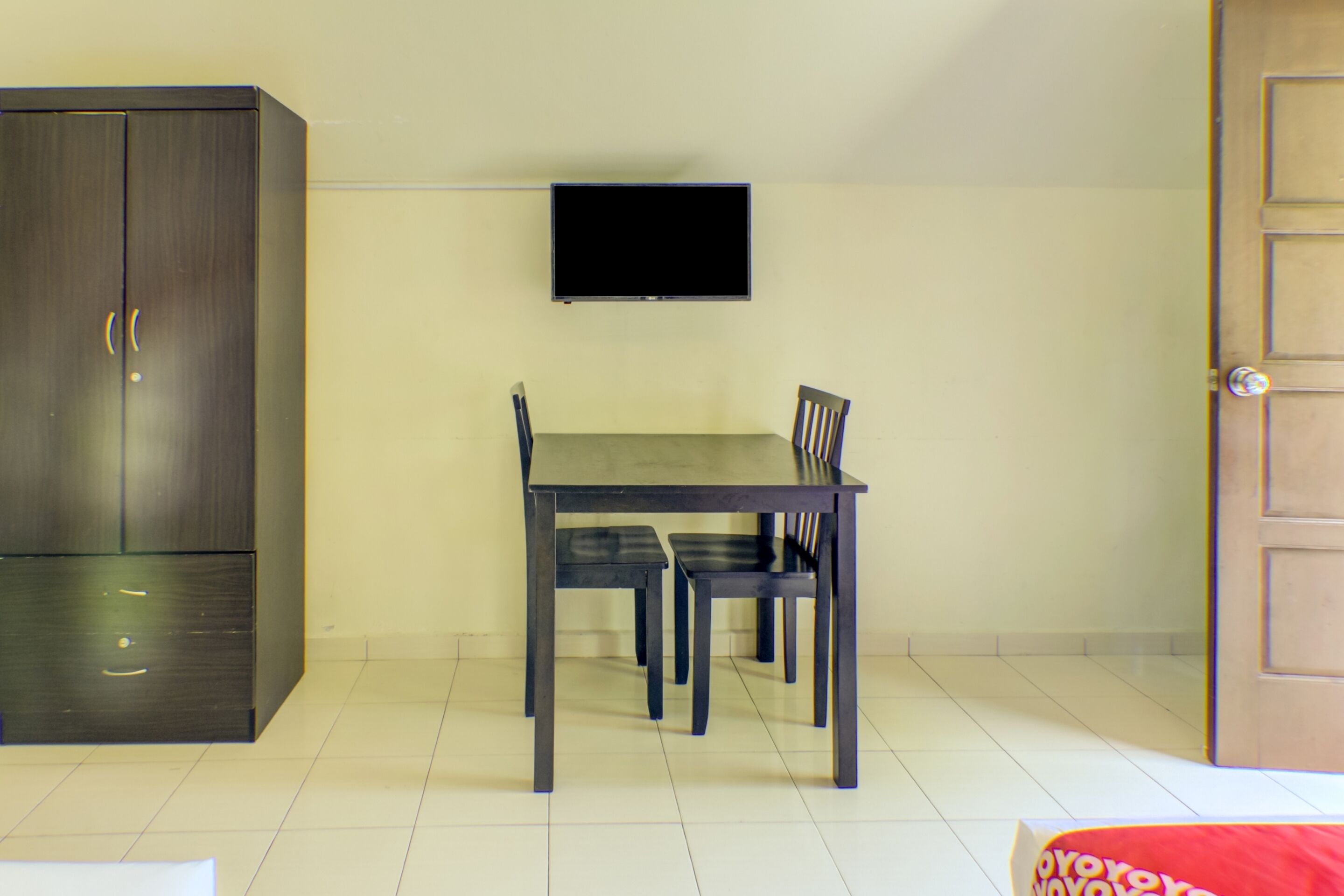 Een kamer met een donkere houten garderobe, een tafel met vier stoelen en een wandgemonteerde flatscreen televisie.