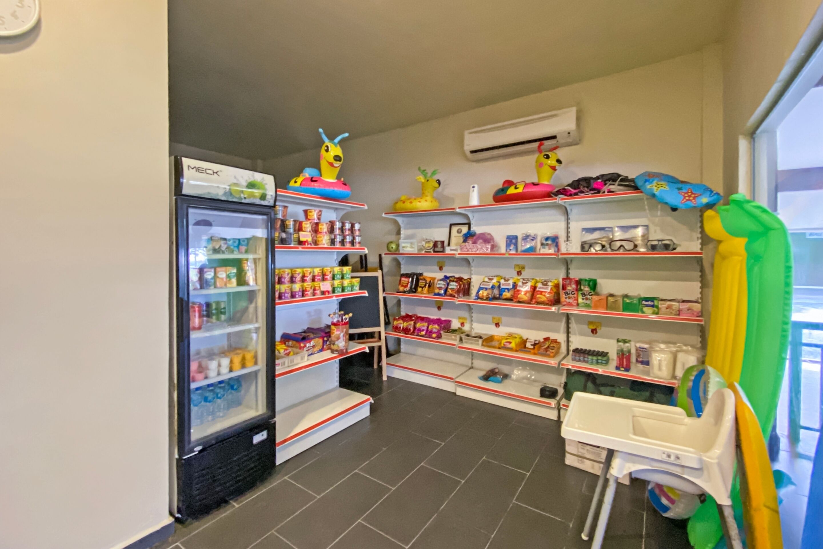 Ein Kinderspielbereich mit Regalen voller Spielzeug und Snacks, einem Kühlschrank und einem kleinen Tisch.