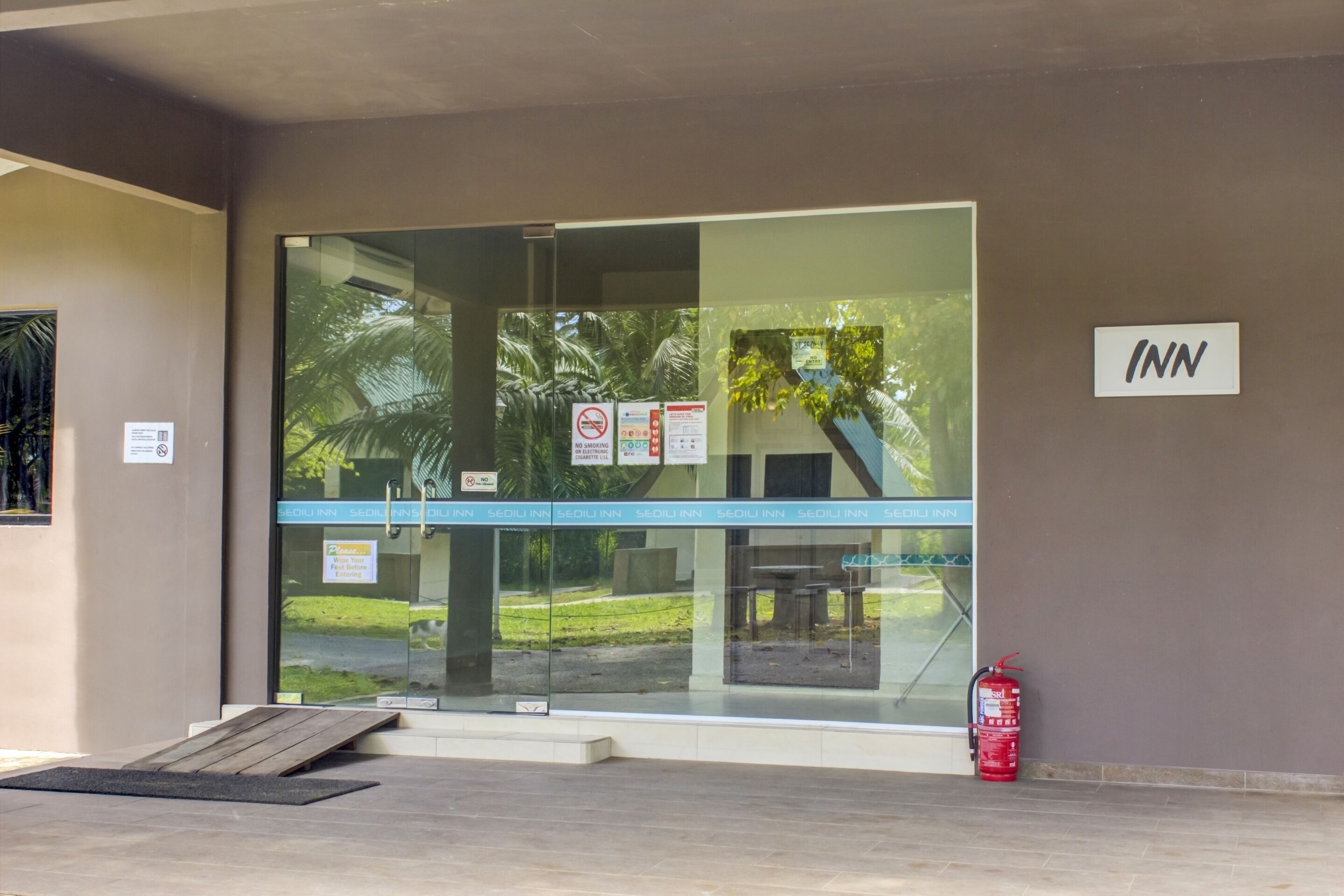 A hotel entrance with a glass door, a fire extinguisher, and a ramp for accessibility.