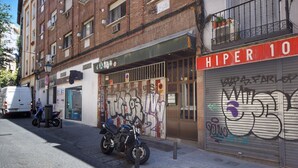 Une vue de rue avec une moto garée devant un immeuble dont le mur est couvert de graffitis et sur lequel on peut lire une enseigne indiquant « HIPER 10 ».