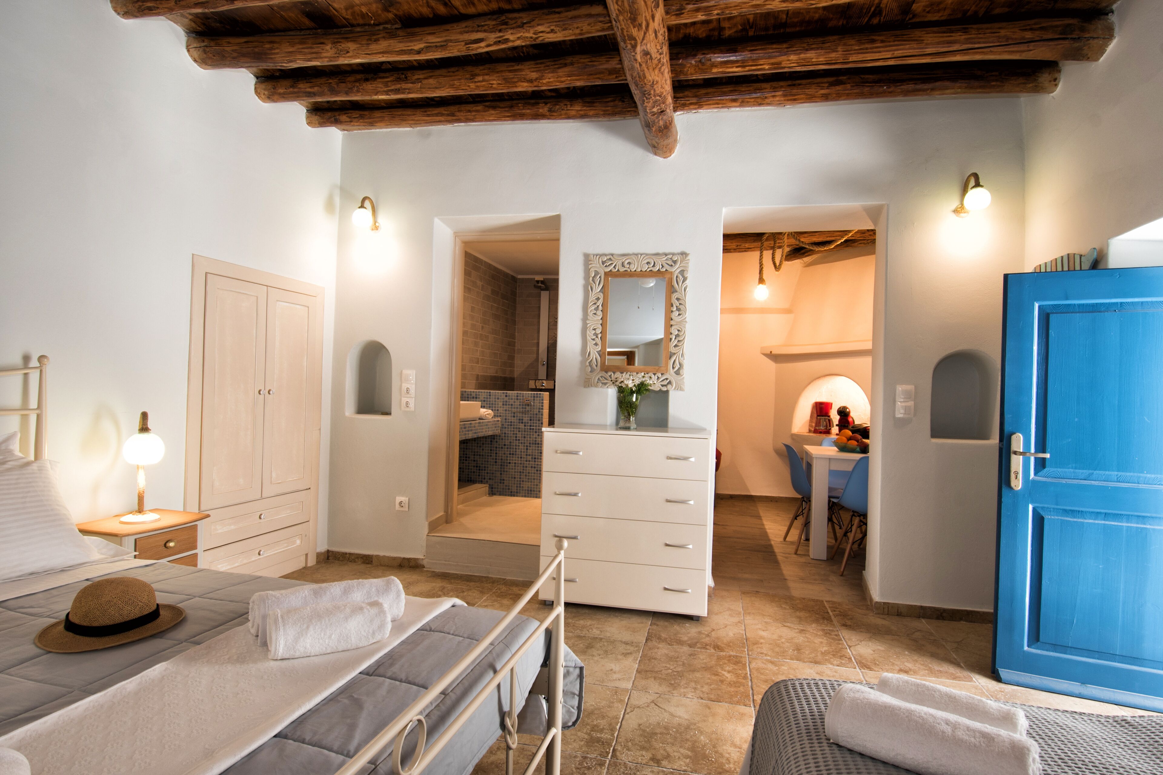 Une chambre à coucher avec un lit, une table de chevet et une armoire. On peut apercevoir une salle de bain à travers une porte ouverte.