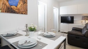 A modern living room with a dining area, a flat-screen TV, and a large painting of a historical building. - Holiday Home Aspalathos, 2 BDR Apt, Close To All Tourist Attractions 		 (Split)