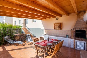 An outdoor patio with a wooden table set for dining, a stone wall, and a brick fireplace.