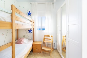 A child's bedroom with bunk beds, a wooden chair, a small desk, and a window with curtains.