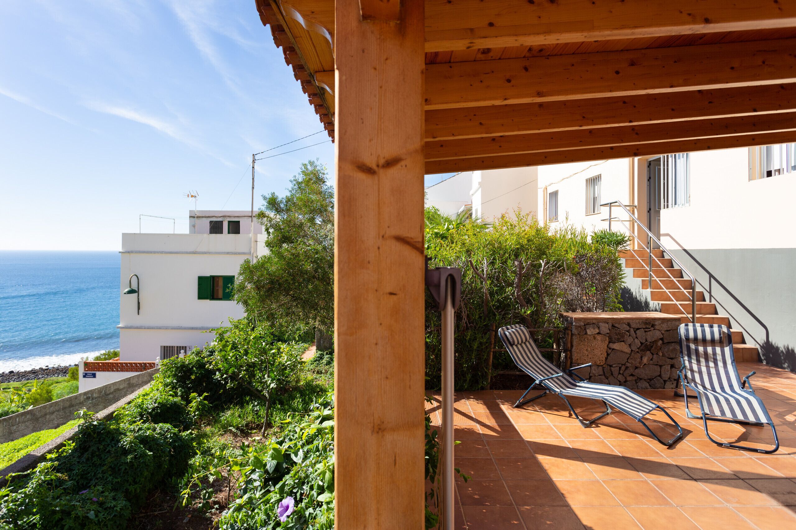 Une pergola en bois avec deux chaises longues, située sur une terrasse carrelée qui offre une vue sur la mer.