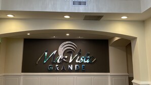A hotel reception area with a chandelier, a sign reading "MarVista Grande," and a wooden floor.