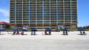 A multi-story hotel with balconies, beach umbrellas, and beach chairs.