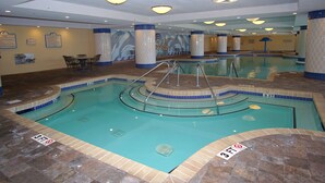An indoor swimming pool with a 3 FT depth marker, tiled walls, and a seating area with tables and chairs.