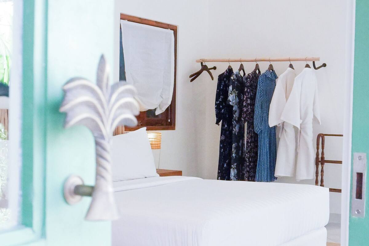 A bedroom with a bed, a wooden headboard, a hanging clothes rack, and a door with a key in the lock.