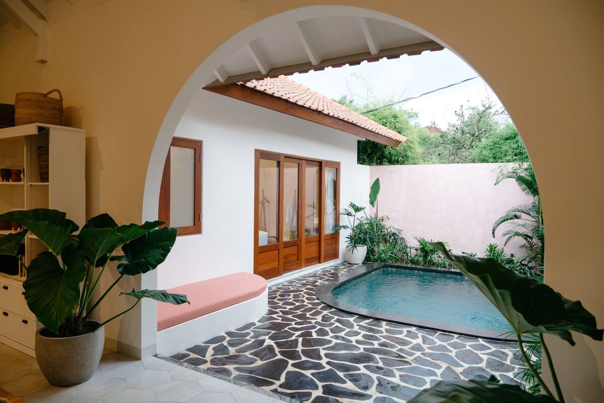 A pool area with stone flooring, a bench, and potted plants.