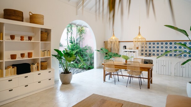 Uma ampla área de refeições com uma mesa e cadeiras de madeira, cercada por prateleiras brancas com livros e cestos.