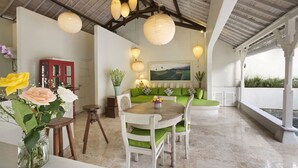 Um quarto espaçoso com teto alto, uma mesa de jantar com cadeiras, um sofá com almofadas verdes e um armário vermelho.