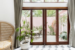 Una habitación con puerta de vidrio corrediza que da a un patio con mesa y sillas, una silla de mimbre y una planta en maceta.
