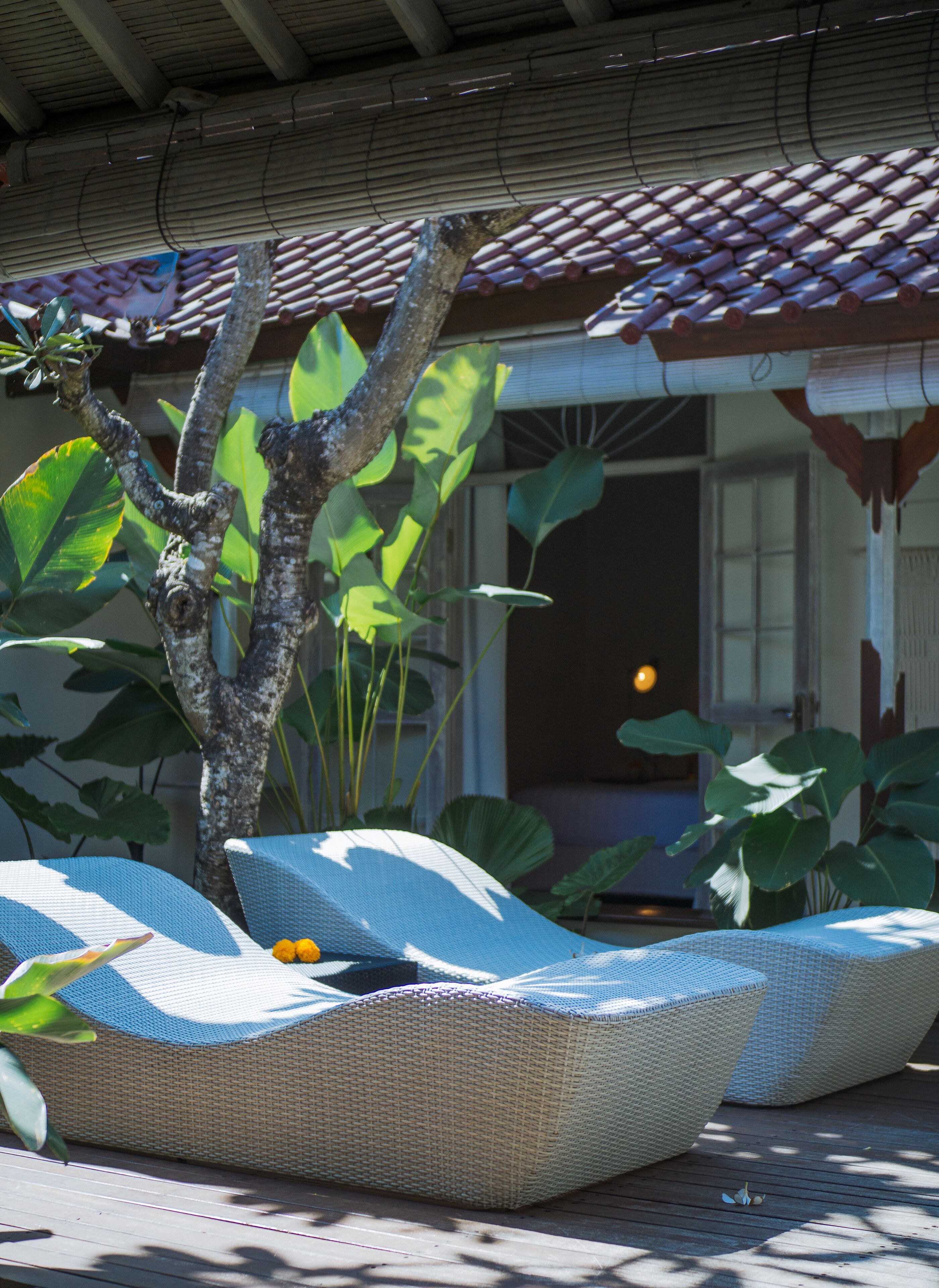 Un espacio de estar techado al aire libre con mobiliario de mimbre y exuberante vegetación tropical.